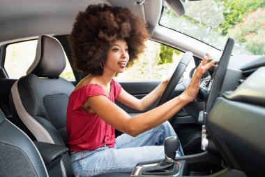 Afro saçlı, gülümseyen Afro saçlı genç bir Amerikalı kadının yan görüntüsü. Şoför koltuğunda otururken ve uydu navigatöründe yön tarif ederken.