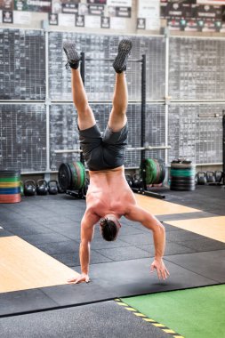 Uzun boylu, şortu olmayan, spor salonunda amuda kalkarak yürüyen güçlü bir erkek.