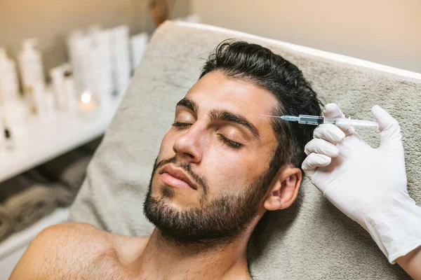 美容院美容师用注射器将肉毒杆菌注入额头时 大胡子男性顾客闭上眼睛 图库图片