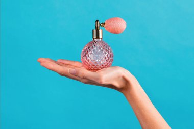 Anonim, zayıf, genç bir kadın, avuç içi klasik kristali tutuyor şeffaf bir şişede klasik bir parfüm kullanıyor ve mavi arka planda üzerine gaz torbası spreyi sıkıyor.