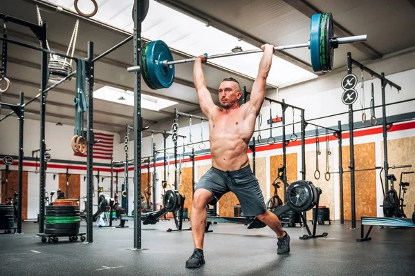 Full body of strong male athlete performing clean and jerk exercise during weightlifting training in gym