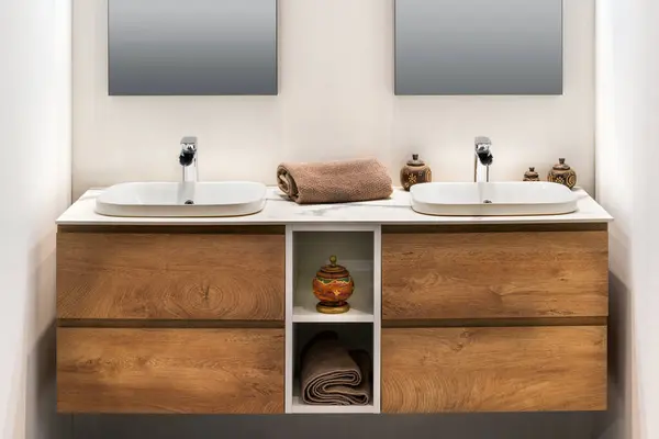 现代最小浴室的内部 双白色洗脸盆水龙头毛巾放在有香炉瓶的木制橱柜架上 镜子固定在白墙上 免版税图库图片