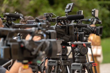 Yazın düzenlenen iş konferansı sırasında doğanın bulanık arka planına karşı tripodlara yerleştirilmiş modern profesyonel video kameralar