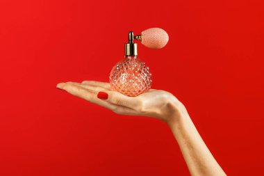 Kırmızı ojeli zarif bir el canlı kırmızı arka planda klasik bir parfüm spreyi sunar.