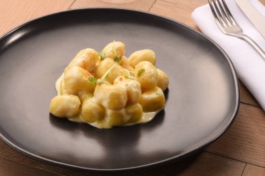 Lokantadaki ahşap masaya servis edilen siyah tabakta beyaz peynir soslu leziz İtalyan gnocchi.