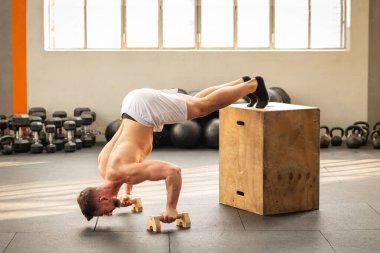 Güçlü kaslı erkeğin beden eğitimi kutusunu açarken yan görünüşü modern spor salonundaki tahta küp üzerinde egzersiz yapması.
