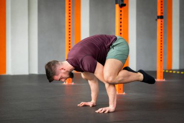 Modern jimnastik salonunda güçlü bir erkeğin beden eğitimi kurbağası standı egzersizi yapmasının yan görünüşü