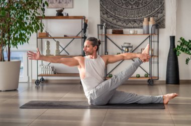 Spor kıyafetli güçlü yetişkin bir erkeğin Devrilmiş Elle Büyük Ayak Parmağı yogası pozu verip salonda egzersiz yaparken yüzünü çevirdiği yan bakış.