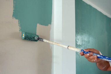 Kimliği belirsiz erkek el, yenileme sırasında metal çubuğun ucuna bağlı paten fırçasıyla duvardaki yeşil rengi boyarken,