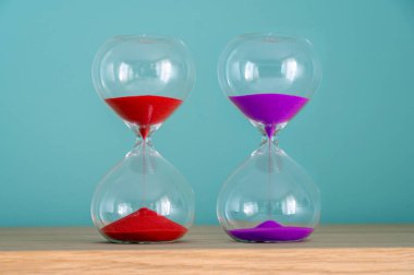 Tahta bir yüzeyde duran iki renkli kum saati geçen zamanı gösteriyor.