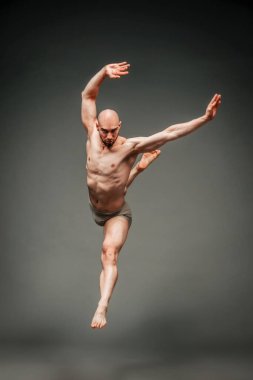 Kaslı kel erkek dansçı, gri bir arka planla zarif bir şekilde stüdyoda zıplıyor.
