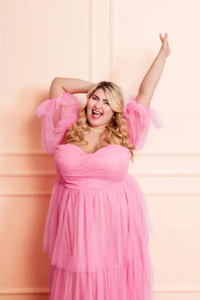 stock image Curvy model posing in pink tulle dress on pink background