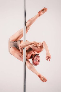 Tam boy, kaslı yetişkin bir adamın zarif bir şekilde direği tutup akrobasi yaparak stüdyoda dayanıklılık ve esneklik sergilediği çekim.