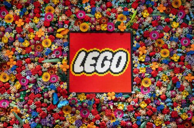 Renkli çiçeklerle çevrili plastik tuğlalardan yapılmış lego logosu da tuğladan yapılmış.