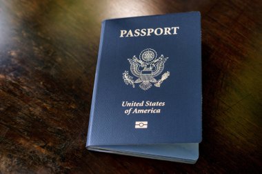 Vatandaş mavi pasaport kitabı altın renkli sembollerle basıldı ve Amerika Birleşik Devletleri kapak sayfasına ahşap rafı yansıtan ışığı yerleştirdi.