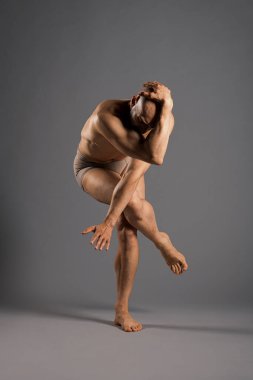 Çağdaş dans pozu veren tişörtsüz bir dansçı bir stüdyo ortamında tek bacağını kaldırıp elini başının üstüne koyuyor.