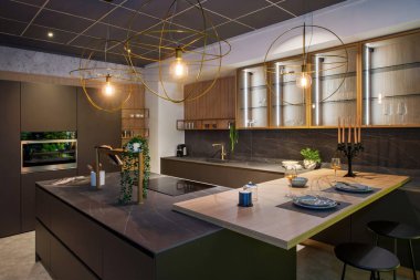 Modern mutfak tasarımı, entegre cihazlar ve küresel kolye ışıklarıyla aydınlatılmış merkezi bir ada.