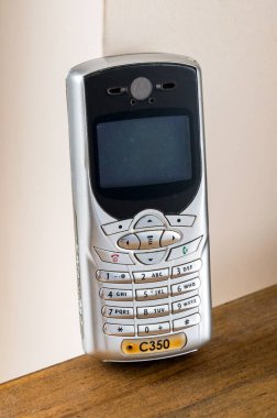 Eski cep telefonu Motorola C350, 2000 'lerden kalma, fiziksel klavyesi ve tahta yüzey üzerinde duran küçük ekranı var.
