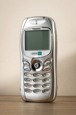Eski gümüş renkli Panasonic GD75 cep telefonu ahşap bir masada duruyor, geçmiş iletişim teknolojisini temsil ediyor.