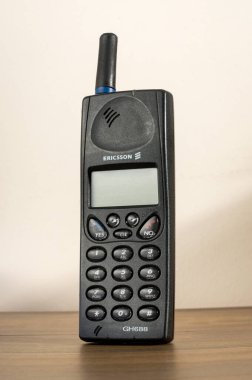Ericsson GH688 model bir cep telefonu ahşap bir masanın üzerinde duruyor ve geçmişten kalma bir iletişim teknolojisini sergiliyor.