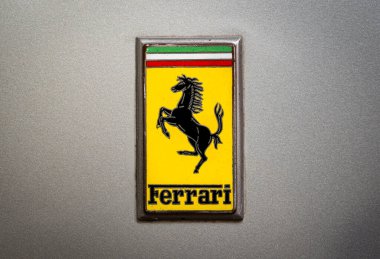 Klasik Ferrari amblemi metalik gümüş bir yüzeyde sergileniyor, sembolik zıplayan atı sergiliyor.