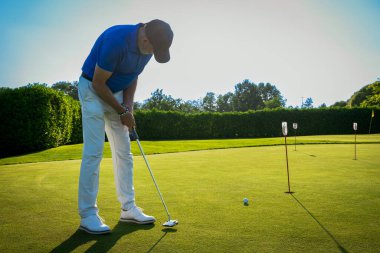Güneşli bir günde golf sahasının yeşilini takan bir golfçü.