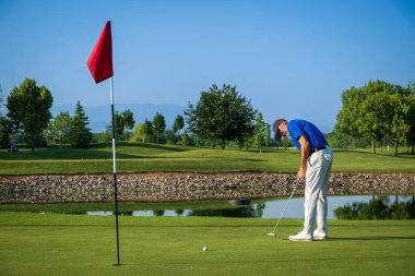 Güneşli bir günde güzel bir golf sahasında golf oynayan kıdemli golfçü, topu yeşile atıyor.