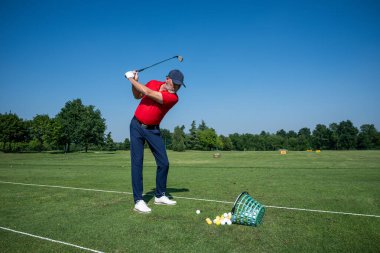 Kıdemli golfçü güneşli bir günde golf sahasında vuruşunu çalışıyor.