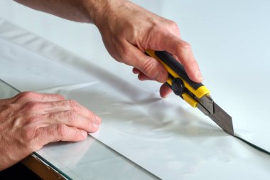 Cam sehpada beyaz vinil yapıştırıcı kesen bir bıçakla ellerini kapat.