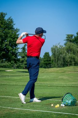 Güneşli bir günde golf sahasında atış talimi yapan profesyonel bir golfçü.