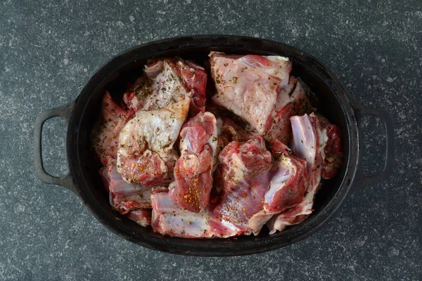 调味羊肉在黑铁锅中 准备烘烤 在黑暗的石头背景之上 顶部视图 — 图库照片