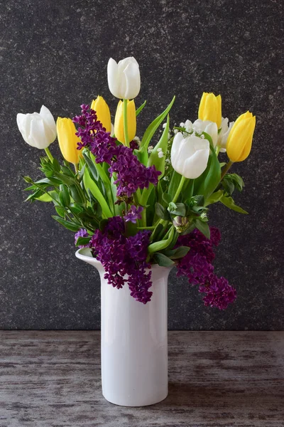 一束美丽的郁金香和紫丁香在一个白色的花瓶里 背景是黑色的石头 侧面看 — 图库照片