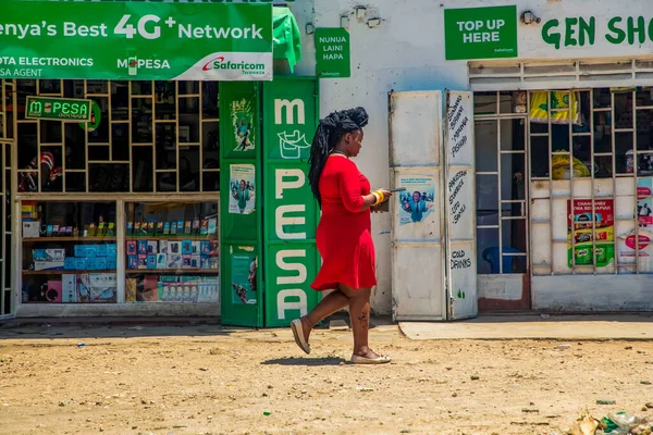 DIani Mombasa Kenya 18 Ekim 2019. Küçük geleneksel Afrika sokak pazarı. Parlak kırmızı elbiseli bir kız dükkanın önünden geçiyor.