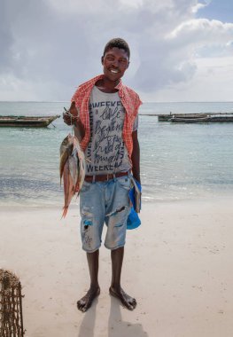 Diani plajı, Mombasa, Kenya. 14 Ekim 2019. Yüzme havuzu, sıcacık beyaz evleri ve tropikal ağaçlarla dolu güzel bir tatil köyü. Okyanus kıyısında balık tutan mutlu bir Afrikalı balıkçı.