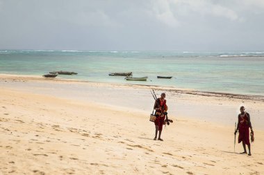 Diani plajı, Mombasa, Kenya. 14 Ekim 2019. Yüzme havuzu, sıcacık beyaz evleri ve tropikal ağaçlarla dolu mutlu Afrikalı maasailer okyanusun kenarında duruyor ve Afrika 'yı elinde tutuyor.