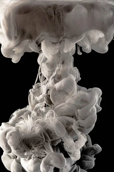 stock image Ink dropped into the water and photographed while in motion. Paint swirling in water. Grey  and white cloud and smoke of paint in water isolated on black background.