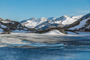 Güneşli bir günde baharın başında Alpler 'de küçük donmuş bir göl. Kar tepeleri, insan yok.. 