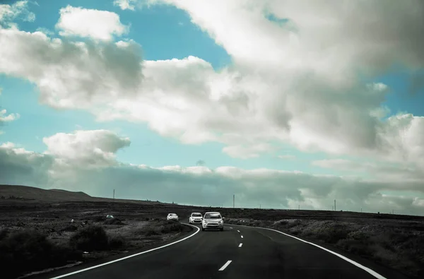 Lanzarote adasında bir yol, mavi gökyüzü, bulutlar ve arabalar geliyor