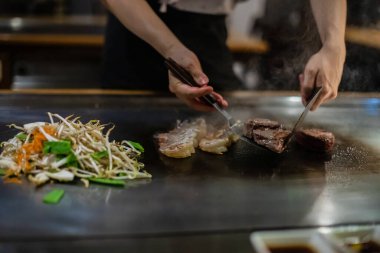 Teppanyaki, geleneksel bir Japon restoranında Japon Teppan Şovu. Aşçının elleri. Japon aşçı sıcak masada et, balık, pirinç ve sebze hazırlar.