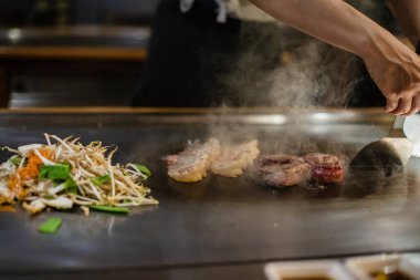 Teppanyaki, geleneksel bir Japon restoranında Japon Teppan Şovu. Aşçının elleri. Japon aşçı sıcak masada et, balık, pirinç ve sebze hazırlar.