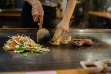 Teppanyaki, geleneksel bir Japon restoranında Japon Teppan Şovu. Aşçının elleri. Japon aşçı sıcak masada et, balık, pirinç ve sebze hazırlar.