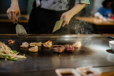 Teppanyaki, geleneksel bir Japon restoranında Japon Teppan Şovu. Aşçının elleri. Japon aşçı sıcak masada et, balık, pirinç ve sebze hazırlar.