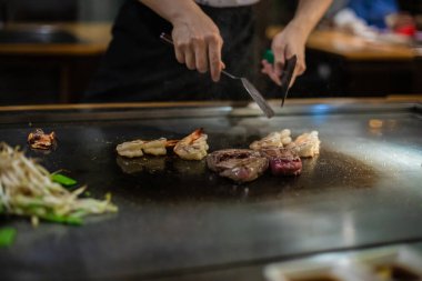 Teppanyaki, geleneksel bir Japon restoranında Japon Teppan Şovu. Aşçının elleri. Japon aşçı sıcak masada et, balık, pirinç ve sebze hazırlar.