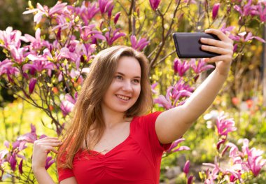 Mutlu genç bir kadın akıllı telefonuyla selfie çekiyor. Cep telefonuna gülümseyen vlogger kızı görüntülü arama yapıyor, manolya arka planında video bloğu çekiyor. Selfie günlük tutma kavramı