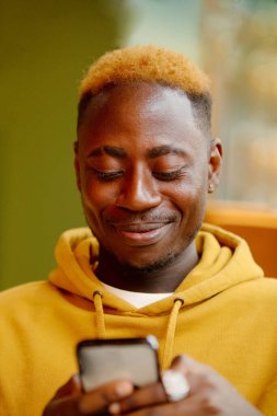 Akıllı telefonlu, sıradan sarı giyinmiş, duygusal, genç bir zenci. Mutlu yakışıklı Afro-Amerikan milenyum adamı iyi duyguları paylaşıyor, uzayı kopyalıyor. Kapat.