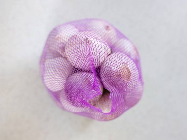 Yüzeyde, leylak rengi plastik bir ağ içinde bir demet çiğ sarımsak solosu var. Üst görünüm çok yakın