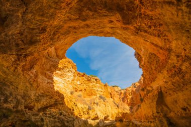 Portekiz Algarve 'nin ünlü mağaraları. Gökyüzünün görüntüsü kayadaki büyük bir delikten geçen bir kuyuya benziyor. Mavi gökyüzü ve kırmızı kayalar. Seyahat kavramı