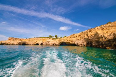 Garip şekiller kabartmalı kil taşlı kızıl uçurum Atlantik okyanus kıyıları güneş Portekiz Algarve ve su üzerinde kayık izleriyle aydınlanıyor..