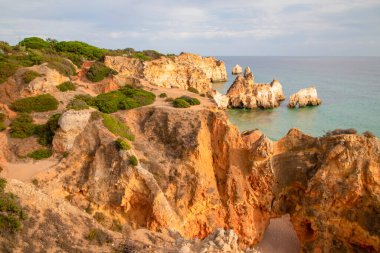 Garip şekiller kabartmalı kırmızı kayalık uçurum, Atlantik okyanus kıyısında güneş Portekiz Algarve 'i aydınlatıyor. Seyahat ve tatil konsepti