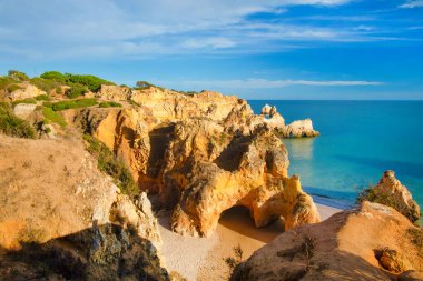 Garip şekiller kabartmalı kırmızı kayalık uçurum, Atlantik okyanus kıyısında güneş Portekiz Algarve 'i aydınlatıyor. Seyahat ve tatil konsepti